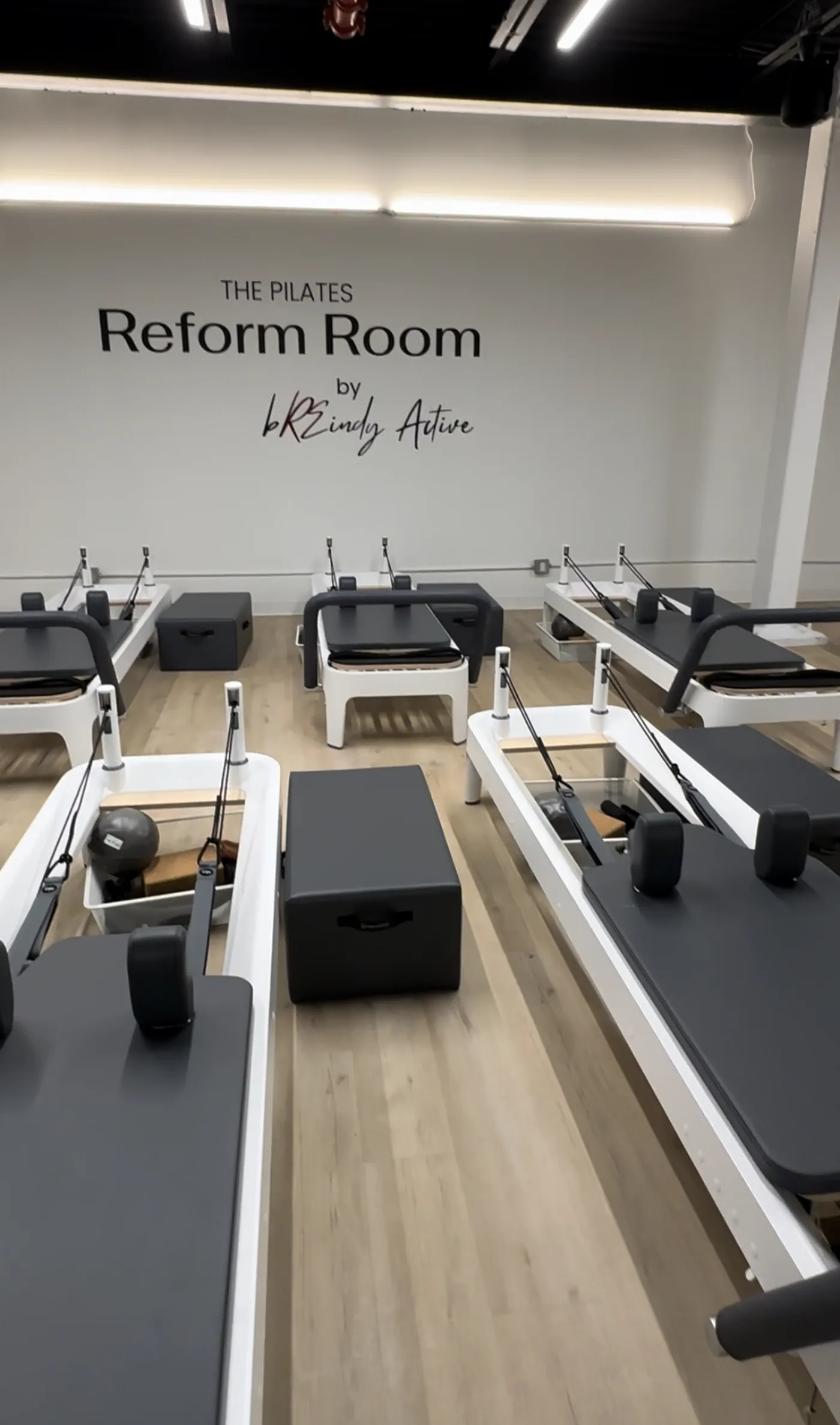 The Reform Room studio filled with Pilates reformers beneath a wall reading The Pilates Reform Room by Breindy Active