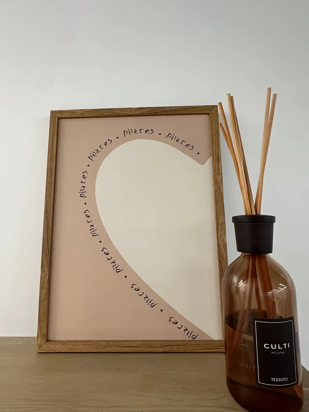 Framed Pilates art print beside a reed diffuser on a wooden shelf